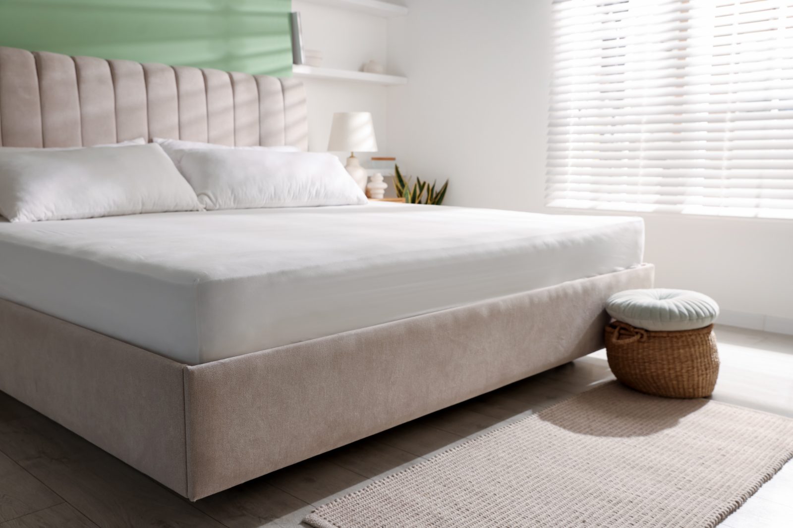 A queen bed made up with a white mattress and pillows against a tall padded headboard, in a bright bedroom.